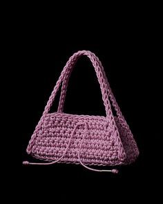 a pink crocheted purse on a black background with the handle extended to it's side