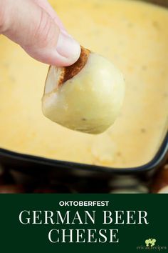 a hand holding a piece of bread over a casserole dish with cheese in it