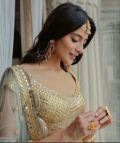 a woman in a gold and white sari is looking down at her wrist bracelet