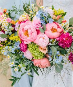 a bride holding a bouquet of pink and blue flowers with greenery in her hands