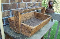 an old wooden box sitting on top of a bench next to a brick wall and green grass