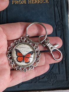 a hand holding a book with a butterfly on it and a key chain attached to it