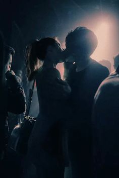 a man and woman kissing in the dark with their arms around each other as people look on