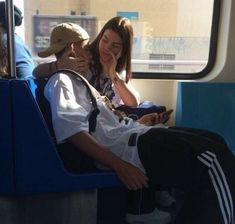 a man and woman sitting on a bus looking at their cell phones while they're talking to each other