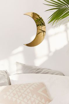 a white bed topped with pillows and a crescent moon hanging from the wall next to a plant