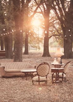 an outdoor seating area with couches, tables and chairs in the woods at sunset