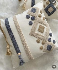 two decorative pillows with tassels and beads on them sitting on a white furnishing