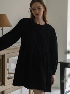 This dress exhibits a relaxed fit with a gathered waistline, creating a flared skirt that enhances its loose silhouette. It features a round neckline and a button-up front, which continues halfway down, providing a balance between structure and ease. The long sleeves are finished with elastic cuffs, adding a slight volume to the arms. The fabric looks soft and possibly lightweight, which contributes to the flowy nature of the dress.- The gathered waistline not only accentuates the dress's shape but also allows for comfortable wear.- With its simple and versatile design, this dress could be accessorized in multiple ways to suit different occasions.- The dress's button-up detail adds a classic touch, while the dark tone gives it an air of sophistication. Long Sleeve Midi Dress With Gathered Waist For Daywear, Long Sleeve Midi Dress With Gathered Waist For Work, Workwear Long Sleeve Midi Dress With Gathered Waist, Smock Dress For Workwear In Fall, Long Sleeve Midi Dress With Gathered Waist, Fall Daywear Dress With Gathered Waist, Fall Smock Dress For Workwear, Fall Workwear Smock Dress, Long Sleeve Smock Dresses For Work