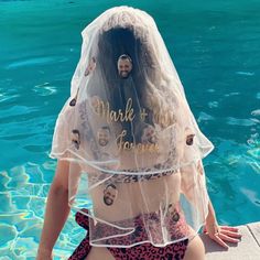 a woman sitting on the edge of a swimming pool wearing a veil over her head