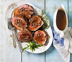 a white plate topped with meat covered in sauce next to a cup of tea and fork