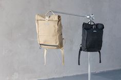 two backpacks are hanging on a clothes line and one is black, the other tan