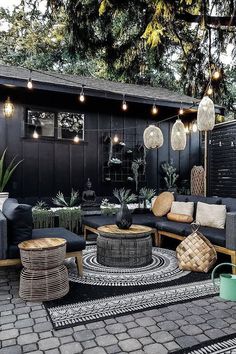 an outdoor living area with black furniture and lights hanging from the ceiling, surrounded by potted plants