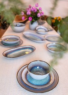 a table topped with plates and bowls filled with flowers on top of a white table cloth