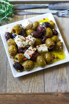 olives with feta cheese and herbs on a white plate next to silverware