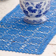 a blue and white doily on a table with a coffee cup in the middle