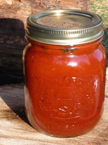 a jar filled with red liquid sitting on top of a piece of wood next to a log