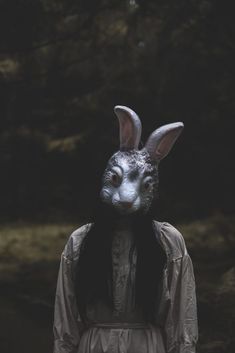 a person wearing a rabbit mask and holding a candle in the woods with trees behind them