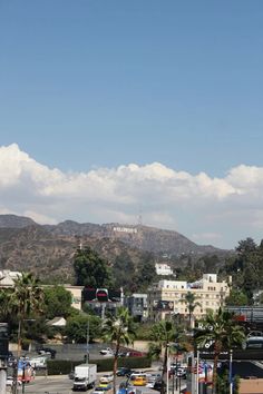 a city with mountains in the background and palm trees on the street below it, as seen from an elevated parking lot