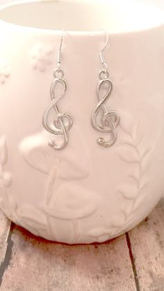 a pair of silver treble earrings sitting on top of a white vase