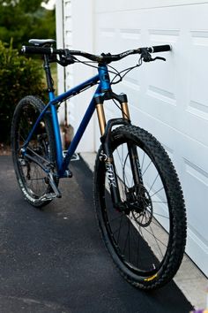 a blue mountain bike parked in front of a garage door next to a flower pot