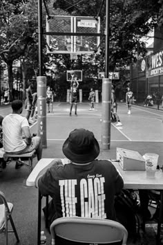 two people sitting at a table on a basketball court while others play in the background