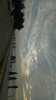 the sky is filled with clouds and some people are walking down the sidewalk in front of it