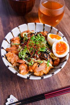 a white bowl filled with food next to chopsticks and a glass of beer