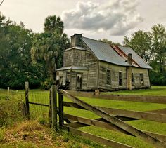 an old run down house sitting in the middle of a lush green field next to a wooden fence