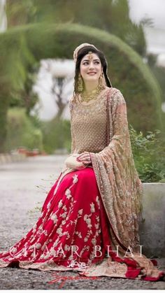 a woman sitting on top of a cement bench wearing a red and gold lehenga