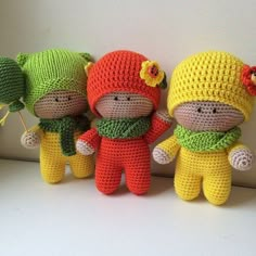 three small crocheted stuffed animals wearing hats and scarves are lined up against a white wall