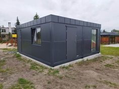 a small gray building sitting on top of a dirt field next to a green yard