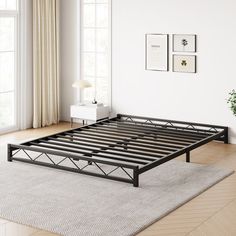 a black metal bed frame sitting on top of a wooden floor next to a window