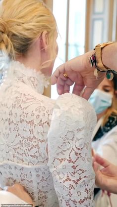 a woman is getting her hair styled by another woman in a white dress and wearing a face mask