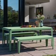 a green table with two benches next to it and flowers in vases on top