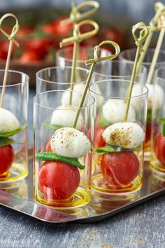 small glass cups filled with mozzarella and cherry tomatoes, topped with green leafy garnish