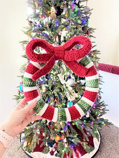 a christmas tree decorated with red, white and green yarn is being held up by a woman's hand