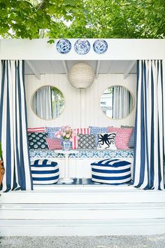 an outdoor seating area with blue and white striped curtains, pillows and mirrors on the wall