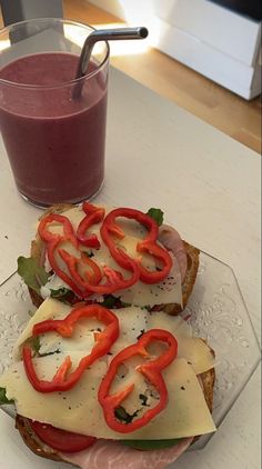 two sandwiches with tomatoes and cheese on them next to a glass of red smoothie