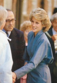 a woman in a blue dress shaking hands with an older man wearing a suit and tie