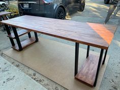 a wooden table sitting on top of a sidewalk next to a parking lot with cars parked in the background