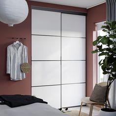 a bedroom with pink walls and white sliding doors, a plant on the floor and a bed in front of it