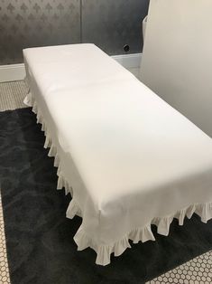 a white bed with ruffles on it in a room next to a wall