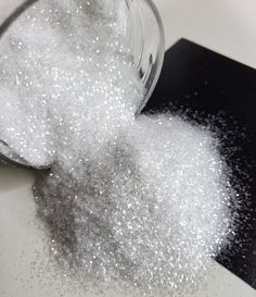 a glass bowl filled with white sugar on top of a black table next to a spoon