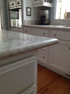 a kitchen with white cabinets and marble counter tops