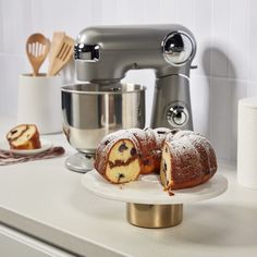 a bundt cake on a white plate with a mixer in the back ground and other kitchen accessories