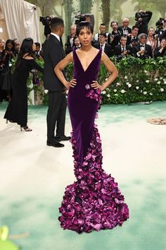 a woman in a purple dress standing on a green carpet with cameras around her and people behind her