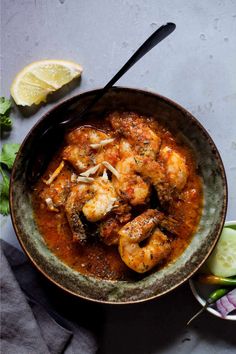 a bowl filled with shrimp and sauce on top of a table next to a lemon wedge