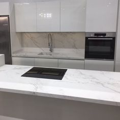 a modern kitchen with marble counter tops and white cabinets, stainless steel appliances and an oven