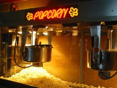 a popcorn machine is lit up with neon lights and popcorn in the bowl on the side