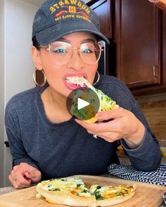 a woman in glasses eating food on top of a wooden cutting board next to a pizza